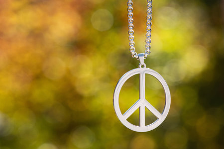 Peace symbol necklace on a green nature bokeh background. sunny weather. bright light. Stop war in Ukraine 2022.の写真素材