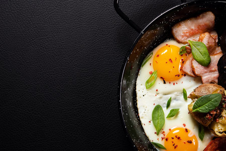 English breakfast with fried eggs and bacon in a black pan background. top view.の写真素材