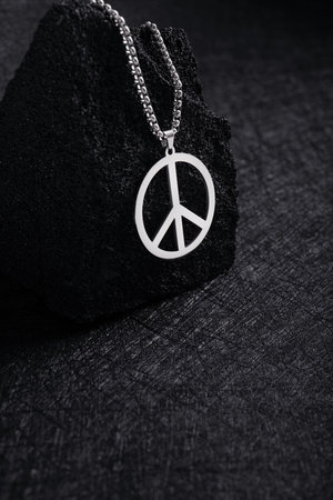 Metal medallion, with a pendant in the form of a mark of peace on a black stone. dark background. concept of freedom. Stop war in Ukraine.の写真素材