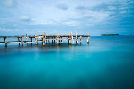 Long exposure photo of a wooden village's bridge on a blue green sea waterの写真素材