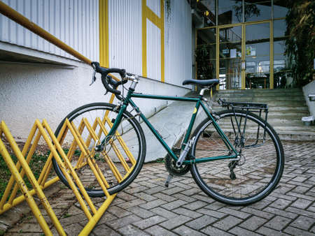Stylist and swift green city bike parking on a yellow rack at the cafeteria's cornerの写真素材