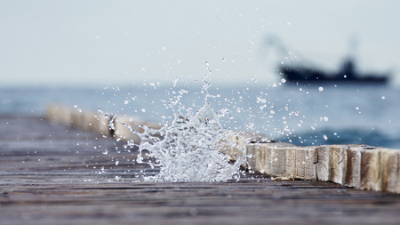 Wooden pier leading into the blue sea and the cascade of sea spray の写真素材