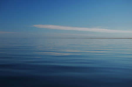 still water into the sea on a background of blue sky and clouds lonelyの写真素材
