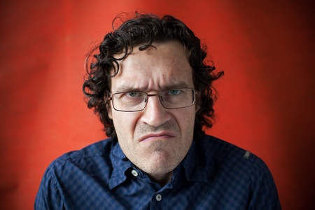 Man wearing glasses with a grimace of displeasure on red backgroundの写真素材