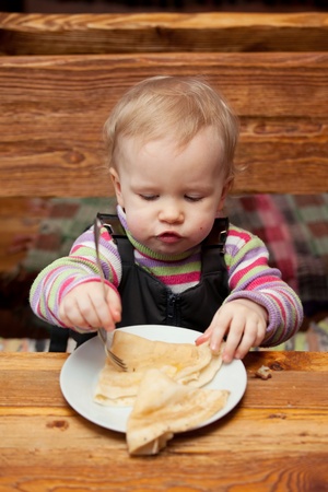 Blond girl eating delicious pancakes on white plateの写真素材