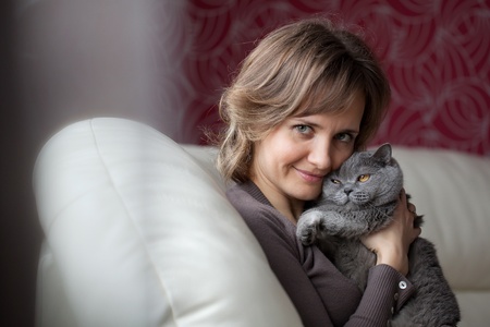 Young woman sitting on the couch and fondles gray catの写真素材