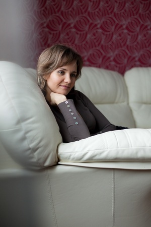 Beautiful young woman settled comfortably on a leather couchの写真素材