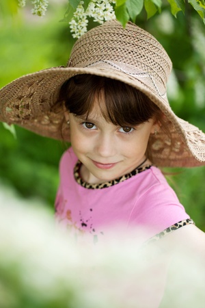 Sweet girl in the hat and the background of a flowering gardenの写真素材