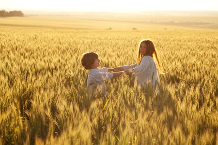 Happy mother and son are running through a wheat field in summerの写真素材