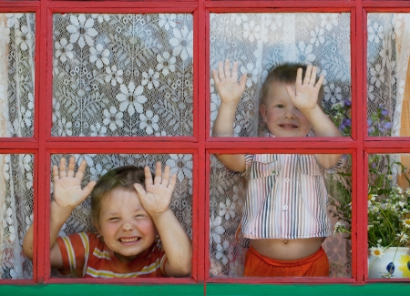 Two kids fool around and show the faces at the windowの写真素材