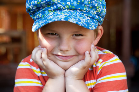 Boy in the blue cap sits cheek propped his hands