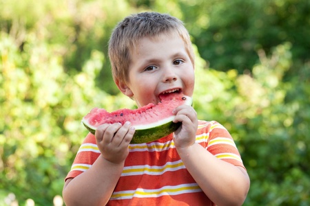 Boy bites off a piece of ripe red watermelonの写真素材