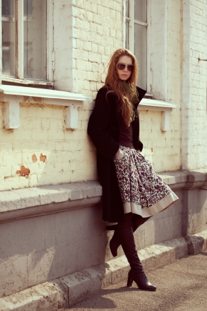 Stylish fashion model in a black coat leaning on a wallの写真素材