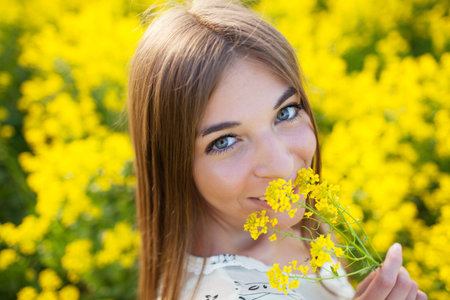 Cheerful girl smelling yellow wildflower summer dayの写真素材