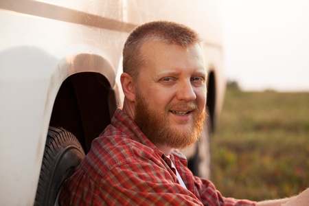Cheerful red-bearded man sitting near the carの写真素材