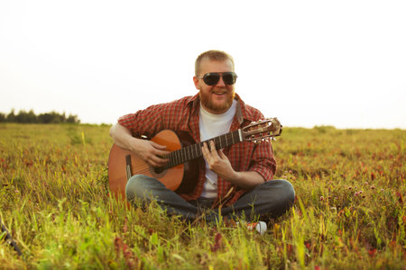 Man in jeans sits on grass and plays guitarの写真素材