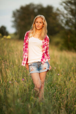 Beautiful blonde girl standing among the grass of the fieldの写真素材