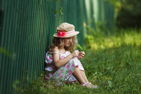 Little girl sits leaning against a fenceの写真素材
