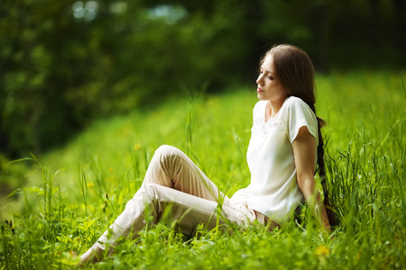 Young pensive woman sitting on the grassの写真素材