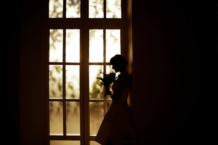 Stylish bride with a bouquet of standing at the windowの写真素材