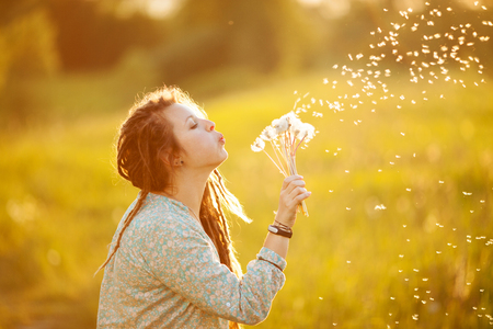 Girl in dreadlocks blowing dandelion on a summer dayの写真素材