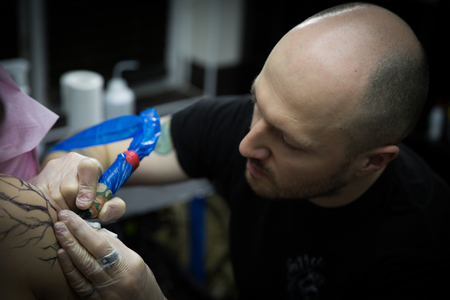 We see a tattoo artist in gloves paint on a man's handの写真素材