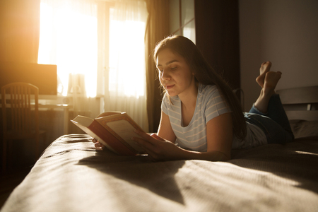 Cute long-haired girl lies and reads a bookの写真素材