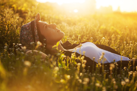 Happy girl in a hat lies among the meadow flowers and dreams of somethingの写真素材