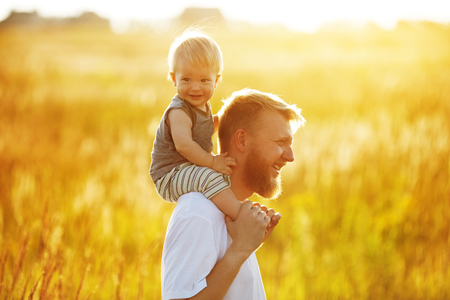 Happy father with his little son on his shoulders in the fieldの写真素材