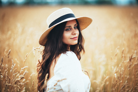 Beautiful young woman in straw hat among field grassの写真素材