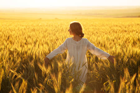 Happy young woman in dress in the middle of a field of ripe ryeの写真素材