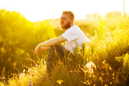Bearded man sits on the grass and looks into the distanceの写真素材