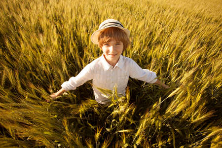 Happy boy with hat in the middle of ripe wheat fieldの写真素材