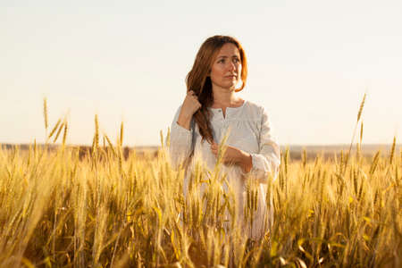 Young long-haired woman stands in the middle of a wheat fieldの写真素材