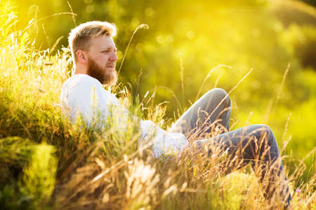 Young man with a beard lies on a summer meadowの写真素材