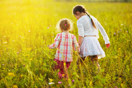 Two little girls are walking in a blooming meadowの写真素材