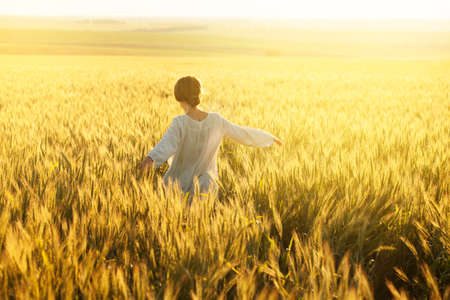 Happy young woman in dress in the middle of ripe wheat fieldの写真素材