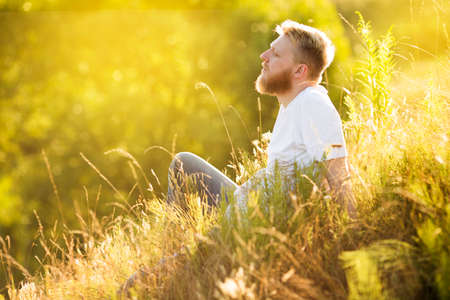 Blonde bearded young man sitting on the grass on a summer dayの写真素材