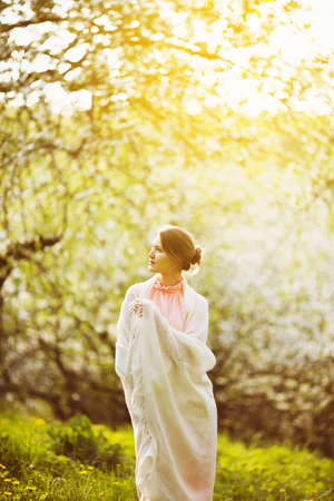 Young woman in a white shawl stands in an apple orchardの写真素材