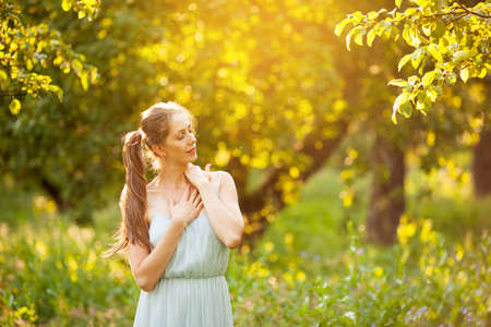 Young happy woman stands with closed eyes in a summer gardenの写真素材