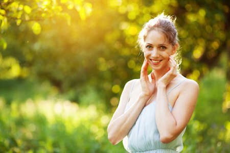 Cheerful young woman in a blue dress in the rays of the evening sunの写真素材