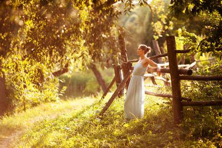 Young woman in a dress is leaning against the hedge in the evening in the gardenの写真素材