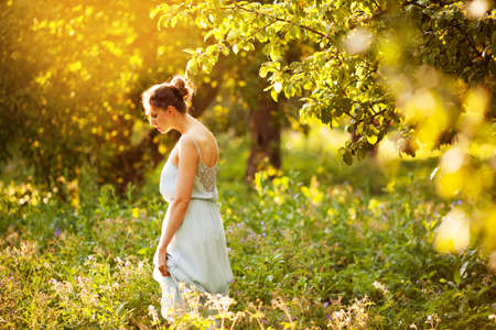 Young woman in a blue dress walks in an apple orchardの写真素材