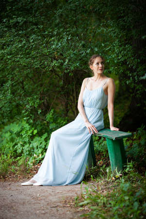 Beautiful young woman in a dress sat down on a park benchの写真素材