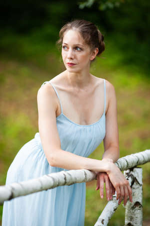 Beautiful young woman in a blue dress leaned on the railing of the bridgeの写真素材