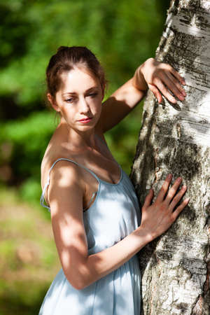 Young pensive woman leaning on a birch tree in the gardenの写真素材