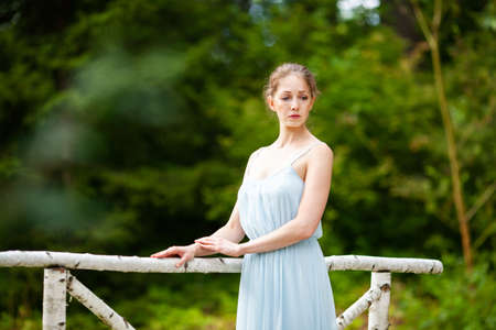 Beautiful young woman in a long blue dress stands on the bridgeの写真素材