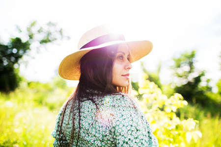 Young woman in hat in the rays of the summer evening sunの写真素材