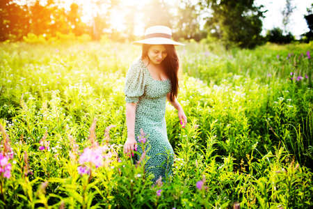 Young woman in a hat walks in a field among flowersの写真素材