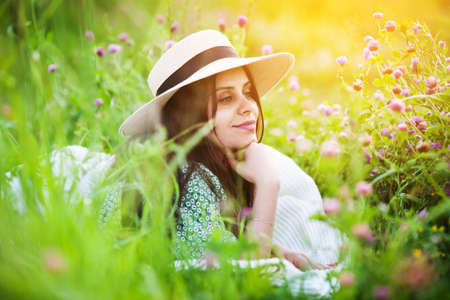 Young woman in a hat lies on the grass among a field cloverの写真素材